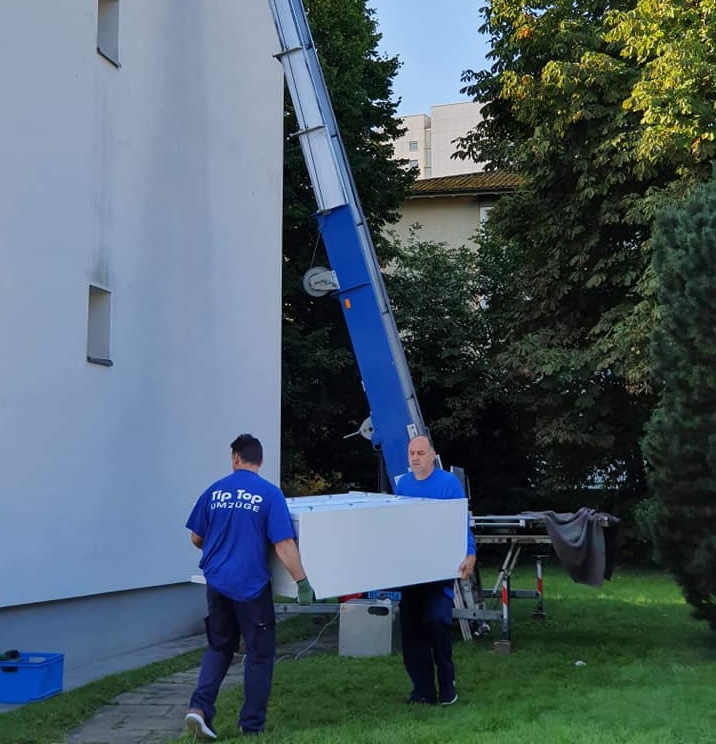 Zwei Mitarbeiter von TipTop Umzüge tragen Möbel bei Umzug in Basel mit Möbellift im Hintergrund